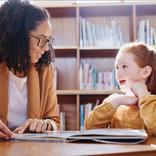 Tutor with student in library looking at book