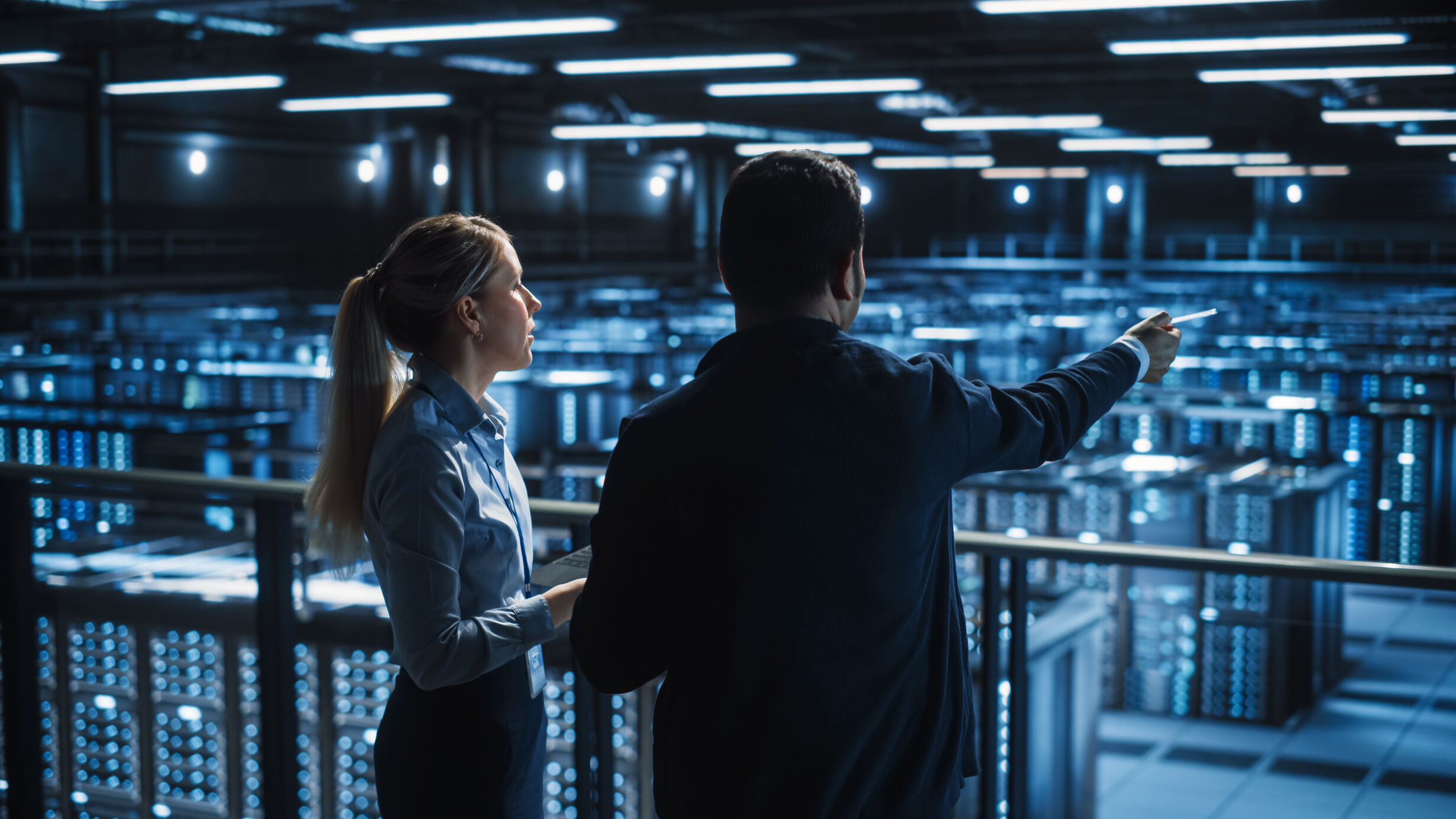 A man and a women looking over a blue tinted data center